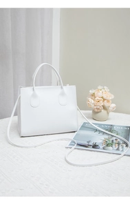 Detailed view of white embroidered faux leather handbag with dual handles on a floral desk