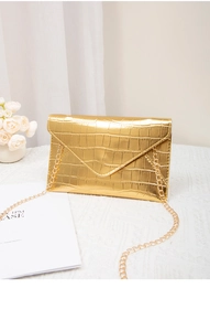 Detail of a golden envelope clutch bag with crocodile texture and thin metal chain