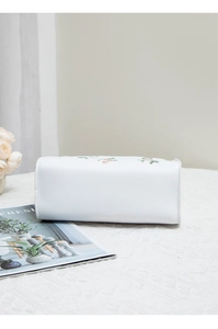 Close-up of elegant floral embroidery on a white PU leather handbag with pink flowers