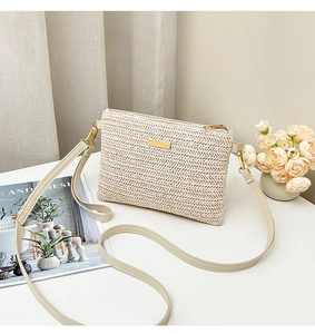 Close-up of cream woven crossbody bag with golden metal logo on a stylish desk