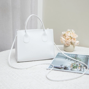 Minimalist white embroidered handbag with top handle and shoulder strap in lifestyle setting