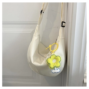 Détail d'un sac bandoulière blanc en demi-lune avec un pendentif tournesol en peluche