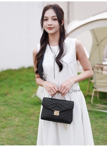 Close-up of black wave-quilted handbag featuring a gold clasp and chain strap on grass