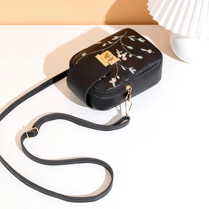 Detailed close-up of floral embroidery and golden metal clasp on black crossbody bag