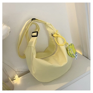 Détail du sac bandoulière jaune en forme de croissant avec texture toile et breloque