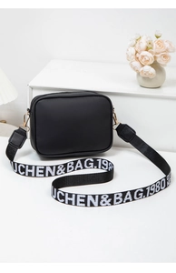Detail of black crossbody bag with logo woven strap and golden metal hardware on white shelf