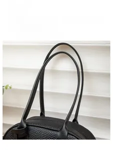 Close-up of black lychee grain leather handbag featuring elongated dual shoulder straps