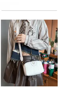 White quilted camera bag with gold butterfly clasp shown on a model in a cozy setting