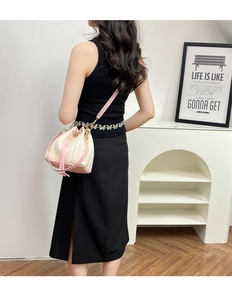 Dettaglio borsa a secchiello in paglia rosa con coulisse indossata da modella in nero