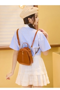 Close-up of small brown leather backpack featuring a vintage triangular design and adjustable straps
