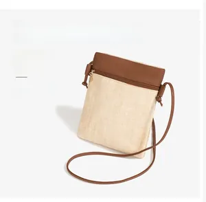 Detailed view of beige woven phone bag with brown leather strap and metal zipper closure
