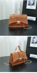 Detail of brown crocodile pattern handbag with gold hardware and chain strap