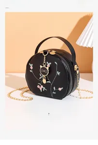 Detail of floral embroidery on a black round crossbody bag with a gold cat pendant