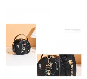 Macro view of floral embroidery and gold cat pendant on black leather round handbag