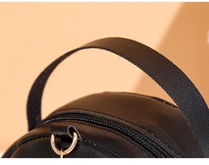 Detailed view of black semi-circular handbag handle with stitching and gold metal ring