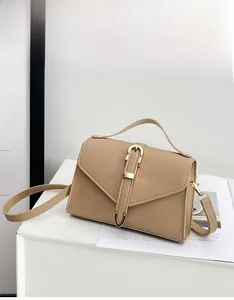 Detail of light brown crossbody bag with V-shaped flap and gold buckle on a white stand