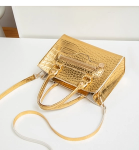 Makroaufnahme der goldenen Krokoprägung und Reißverschlussdetails an der Handtasche