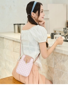 Detail of pink monogram phone bag with pearl pendant and golden cat buckle in a cafe