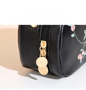Close-up of floral embroidery on black leather bag with a golden metal zipper puller