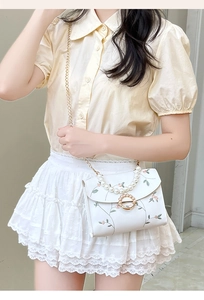 Close-up of pearl handle and floral embroidery on a white crossbody bag with chain