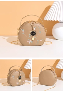 Detailed close-up of floral embroidery and cat-shaped metal charm on round bag