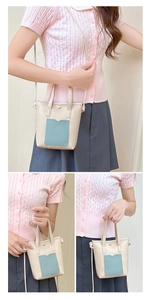 Détail du sac bandoulière crème avec poche bleue, doubles poignées et sangle en cuir