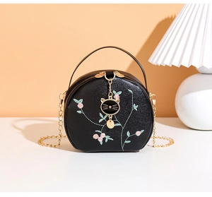 Detail of floral embroidery and gold cat pendant on a round black leather bag