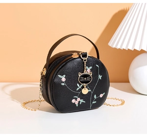 Close-up of black round bag featuring floral embroidery and cat head metal pendant