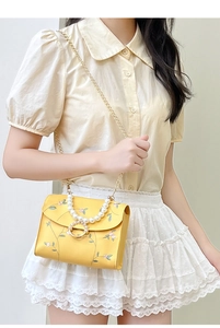 Close-up of yellow crossbody bag featuring floral embroidery and elegant pearl handle