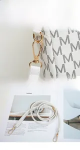 Detail view of white monogram crossbody bag featuring gold-tone hardware and M-print texture