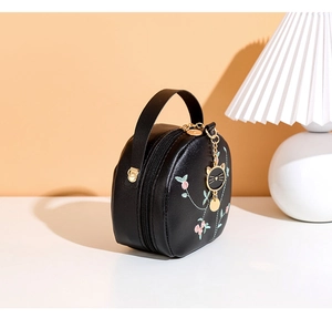 Detail of floral embroidery and gold cat charm on a black round PU leather handbag