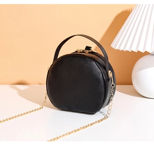 Detail of black round crossbody bag featuring gold hardware and grainy PU leather texture