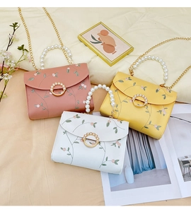 Detailed embroidery on flap of pearl handle crossbody bags in pink, yellow, and white