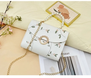 Detail of white embroidered square bag with pink flowers and pearl handle on quilted background