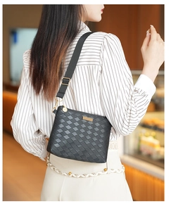 Detail of black woven texture crossbody bag with adjustable strap and gold metal hardware