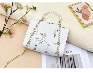Detail of white embroidered flower handbag with luxury pearl handle and gold chain