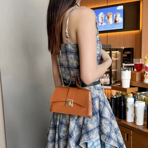 Elegant brown crocodile texture handbag with gold buckle and chain strap on a cafe table