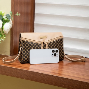 Brown crossbody phone bag with geometric pattern and gold zipper on a wooden desk