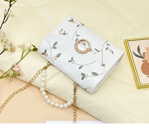 Detail of white embroidered floral bag with pearl handle and golden chain strap