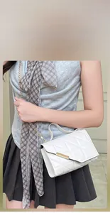 Detail of white quilted handbag featuring a gold metal bar lock and chain shoulder strap
