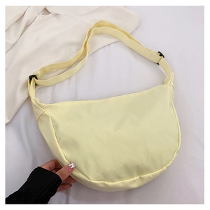 Détail de la texture en nylon jaune crème et de la bandoulière noire réglable du sac à main