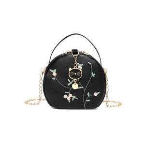 Black round crossbody bag with floral embroidery and golden cat charm on white background