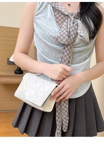 Detailed close-up of a white quilted crossbody bag with golden chain and metal accents