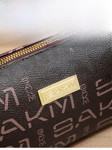 Close-up of brown litchi pattern leather clutch with gold zipper and metal logo plate