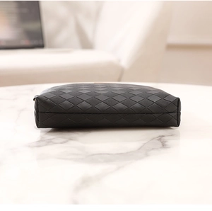 Detail view of a black quilted envelope bag featuring diamond patterns on a marble surface