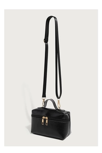 Detail of black oil-wax leather handbag showing gold zippers and adjustable shoulder strap