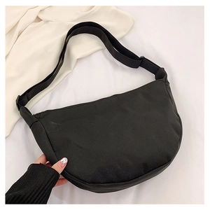Détail d'un sac demi-lune en toile noire avec bandoulière réglable sur tissu blanc