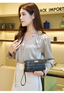 Close-up of vintage patterned clutch bag with gold logo and black wristlet strap