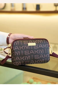 Detail of dark brown leather crossbody bag with letter pattern and golden logo hardware