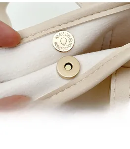 Gros plan sur la boucle magnétique dorée d'un sac à main seau en cuir crème minimaliste